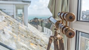 Un telescopio sobre un trípode junto a una ventana con vistas al paisaje costero.