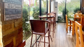 A restaurant interior with wicker chairs, a brick wall, and a large window offering a view of palm trees. - Eduardo's Resort (Calapan)