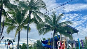 A swimming pool surrounded by palm trees and a water park with slides. - Eduardo's Resort (Calapan)