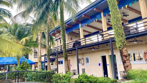 A hotel with a pool, palm trees, and a covered area with blue canopies. - Eduardo's Resort (Calapan)