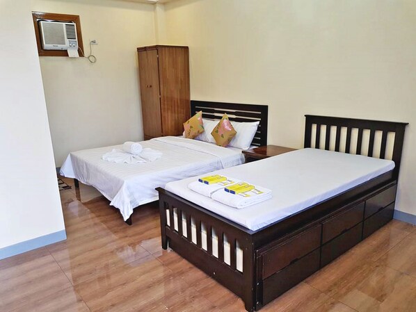 Habitación de hotel con dos camas individuales, un armario de madera y un equipo de aire acondicionado en la pared.