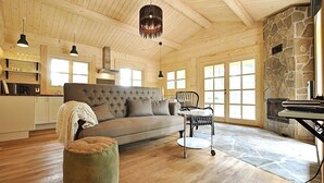 Een ruime woonkamer met een grote bank, een rond hocker, een eettafel met stoelen en een stenen openhaard.