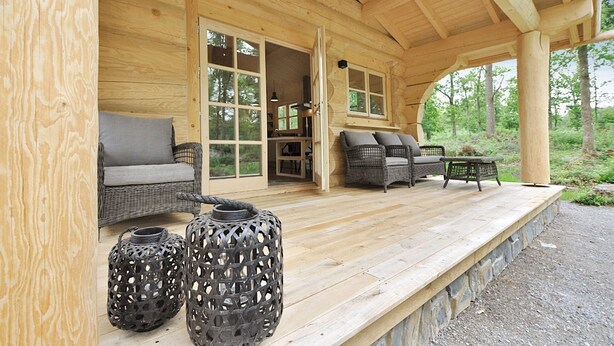 Een houten hut met een overdekte veranda, rieten meubels en twee decoratieve lantaarns.