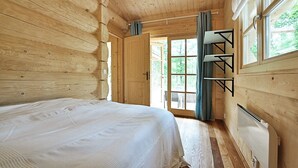 Een houten slaapkamer met een bed, een raam met gordijnen en een inbouwplank.