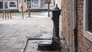 A narrow street with a brick building, a wooden stool, and a metal bollard.