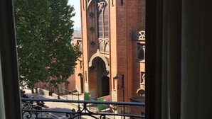 Vista de una iglesia con un campanario alto y ventanas en arco, visible a través de una ventana con barandilla de hierro decorativa.