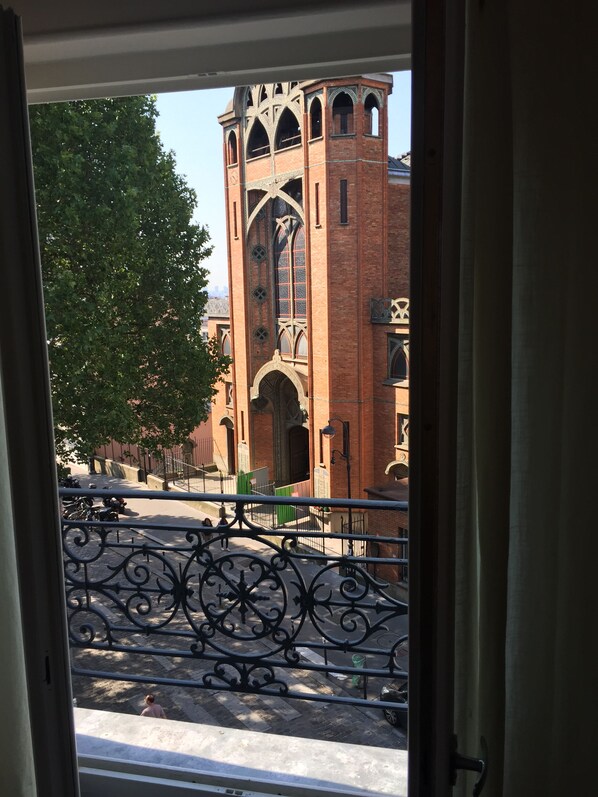 A view of a church with a tall bell tower and arched windows, seen through a window with a decorative iron railing.