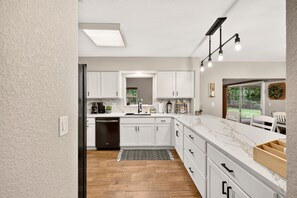 A modern kitchen with white cabinetry, a black dishwasher, and a marble countertop.
