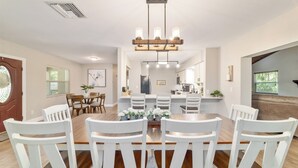 A dining area with a large wooden table surrounded by white chairs, a chandelier, and a view into the kitchen. - 3/2 NEWLY REMODELED HOME IN CRYSTAL RIVER! Bring your boat and RV/Camper!  (Crystal River)