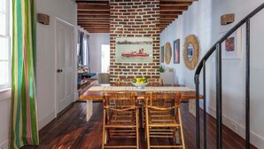 A dining area with a brick wall, wooden ceiling beams, and a table set for four. - Casa Zoë | Cabana House – Bold Design, Prime Location (Charleston)