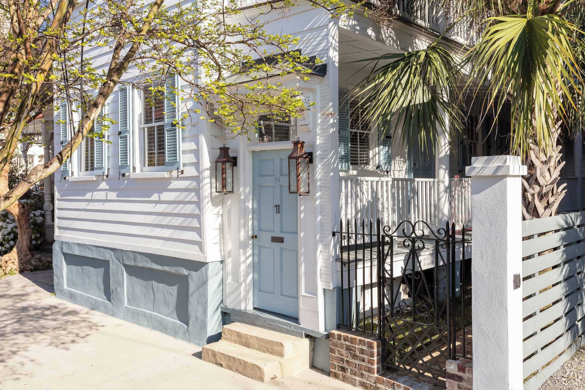 A white building with a light blue door, a small porch, and a black wrought iron gate.