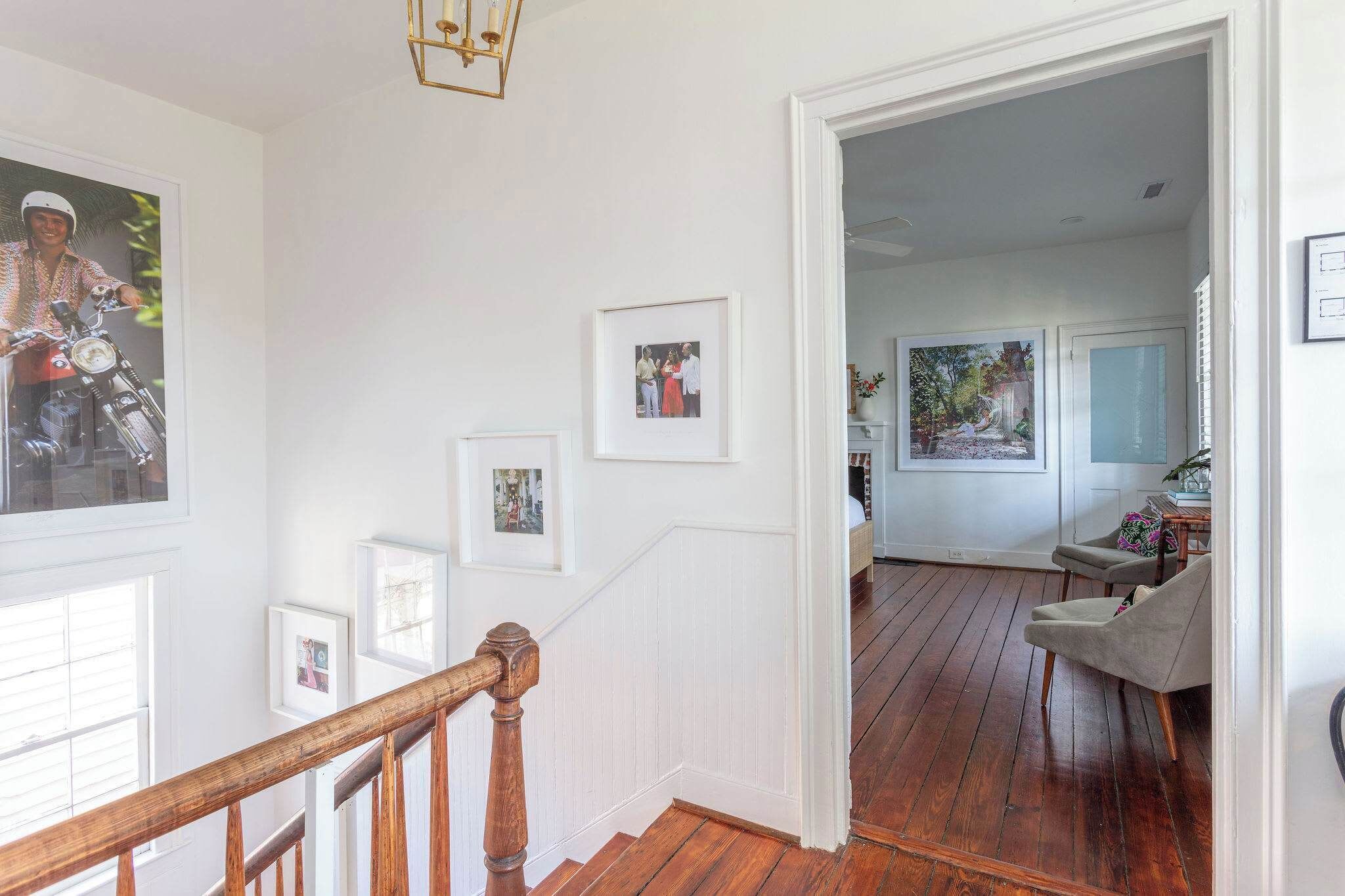 A staircase with wooden railings leading to a room with a wooden floor, white walls, and framed pictures.