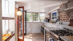 A kitchen with a large window, a brick wall, a gas stove, and a wooden bar stool.