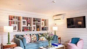 A living room with a blue sofa, a pink armchair, a coffee table, and a bookshelf with various items.
