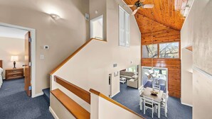 Un intérieur à plusieurs niveaux, avec un escalier, un coin repas comprenant une table et des chaises, et une vue sur l’extérieur.