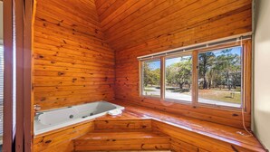 L’intérieur d’un chalet en bois comprend une baignoire, une fenêtre donnant sur les arbres et un plancher carrelé.