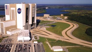 An aerial view of a facility with a large building featuring a NASA logo, adjacent parking areas, and a winding road leading to a body of water. - Quiet Gulf Canal Neighborhood with Enclosed Lanai & Heated Pool EV friendly (Hudson)