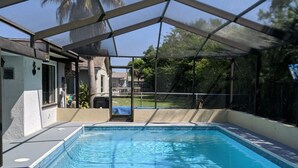 A swimming pool with a clear view of the surrounding area, including a covered patio and palm trees. - Quiet Gulf Canal Neighborhood with Enclosed Lanai & Heated Pool EV friendly (Hudson)