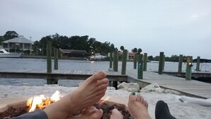 A person relaxing by a fire on a dock with a body of water and boats in the background. - Quiet Gulf Canal Neighborhood with Enclosed Lanai & Heated Pool EV friendly (Hudson)