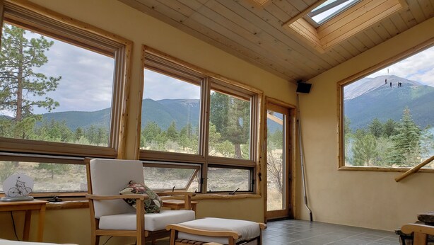 A room with large windows, wooden furniture, and a view of mountains. - Luxury Log Home at Foot of Mt. Princeton (Buena Vista)