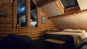 A cozy log cabin bedroom with a large window, a bed, a small table, and a bench. - Luxury Log Home at Foot of Mt. Princeton (Buena Vista)