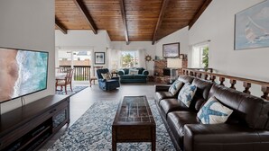 A spacious living area with a wooden ceiling, a large flat-screen TV, a leather sofa, a coffee table, and a fireplace. - 116S Stranded at the Beach (Oxnard)