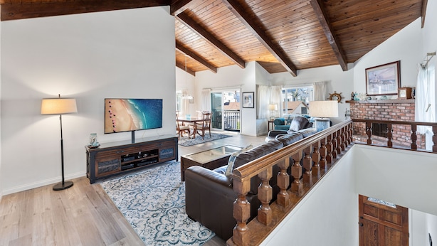 A spacious living room with a high ceiling, wooden beams, a large TV, a sofa, and a staircase with a wooden railing. - 116S Stranded at the Beach (Oxnard)