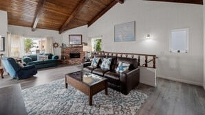 A spacious living room with a fireplace, leather sofas, a wooden ceiling, and a large window. - 116S Stranded at the Beach (Oxnard)