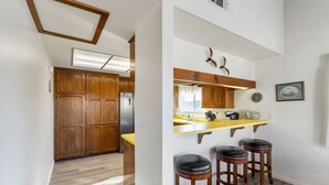 A kitchen with wooden cabinets, a yellow countertop, and two stools. - 116S Stranded at the Beach (Oxnard)