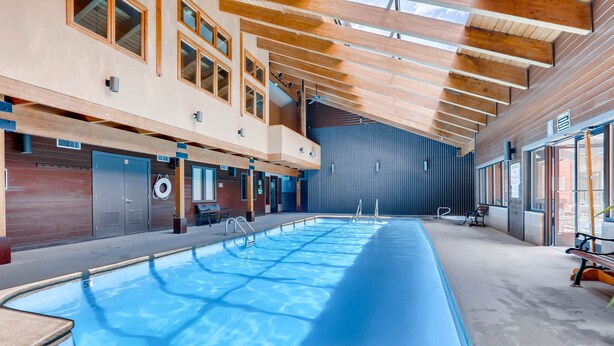 Una amplia piscina interior con techo y paredes de madera, rodeada de zonas de estar y vistas al exterior.
