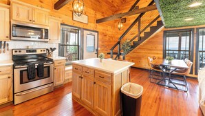 A wooden cabin interior with a kitchen, dining area, and a staircase with a green wall. - Sunset Ridge cabin 21 miles from Chatt, TN! Indoor pool & hot tub! (Bryant)