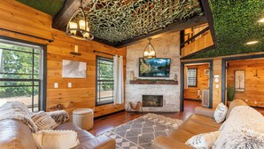 A cozy log cabin interior with a fireplace, wooden walls, and a large window. - Sunset Ridge cabin 21 miles from Chatt, TN! Indoor pool & hot tub! (Bryant)