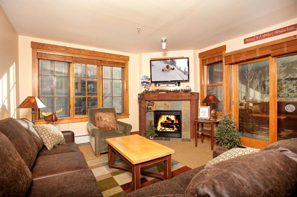 A cozy living room with a fireplace, a television, and a large window with wooden frames.