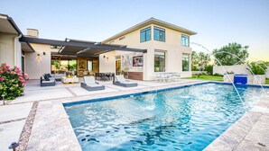 Una casa moderna con piscina, mobiliario de exterior y un porche cubierto.