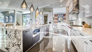 Una cocina moderna con una isla grande, electrodomésticos de acero inoxidable e iluminación colgante.