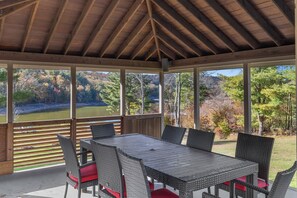 A covered patio with a wooden ceiling, a table with wicker chairs, and a view of a golf course and trees. - Lakefront Paradise: Views, Heated Pool, Games! Summer & Winter Fun For Everyone! (Monticello)