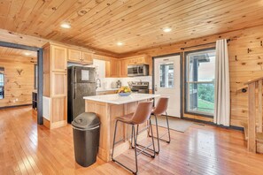 A modern kitchen with wooden cabinets, a central island, and a view through a glass door. - Pop & Granny's cabin with a fire pit, hot tub, & indoor pool! (Bryant)