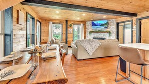 A wooden interior with a dining area, sofa, and TV mounted on a stone wall. - Pop & Granny's cabin with a fire pit, hot tub, & indoor pool! (Bryant)