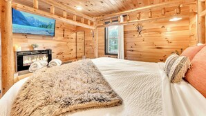 A cozy wooden cabin room with a bed, a fireplace, a TV, and a window. - Pop & Granny's cabin with a fire pit, hot tub, & indoor pool! (Bryant)