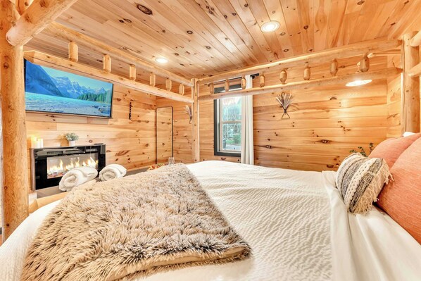 Ein gemütliches Holzhütten-Zimmer mit einem Bett, einem Kamin, einem Fernseher und einem Fenster.