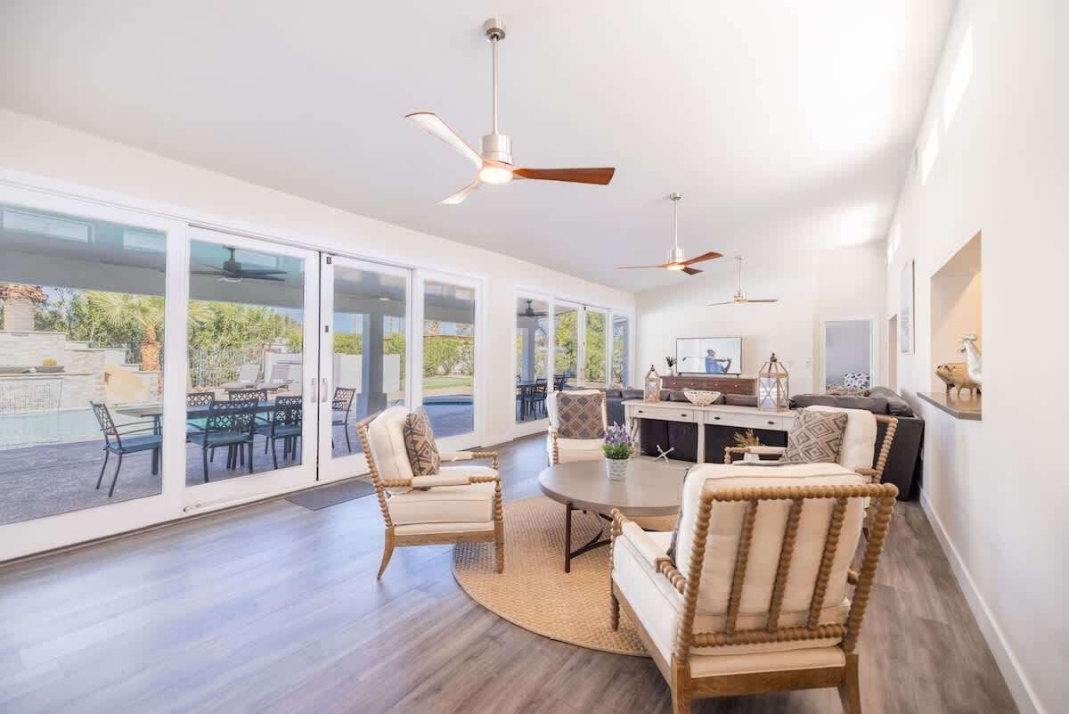 A spacious living area with a large glass door leading to a pool, ceiling fans, and a central coffee table.