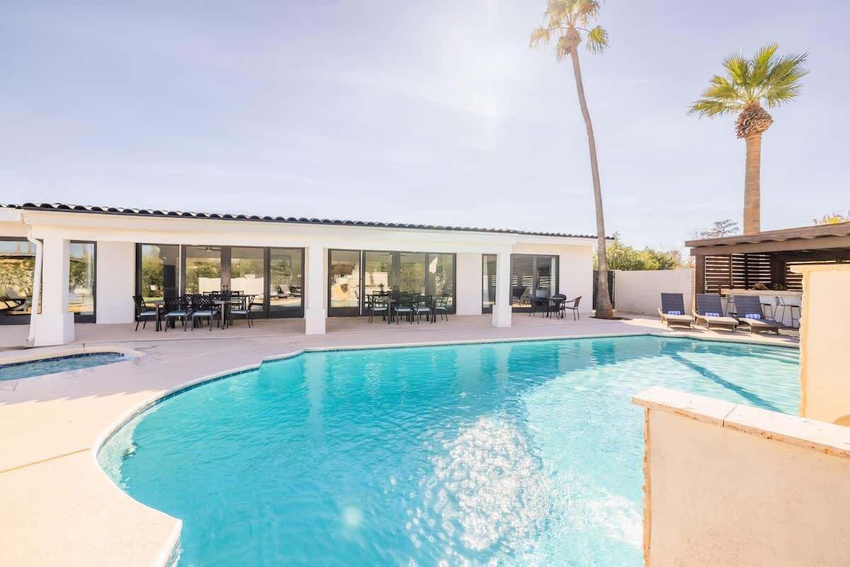 Piscina com borda curva, rodeada por um alpendre coberto com mesas e cadeiras.