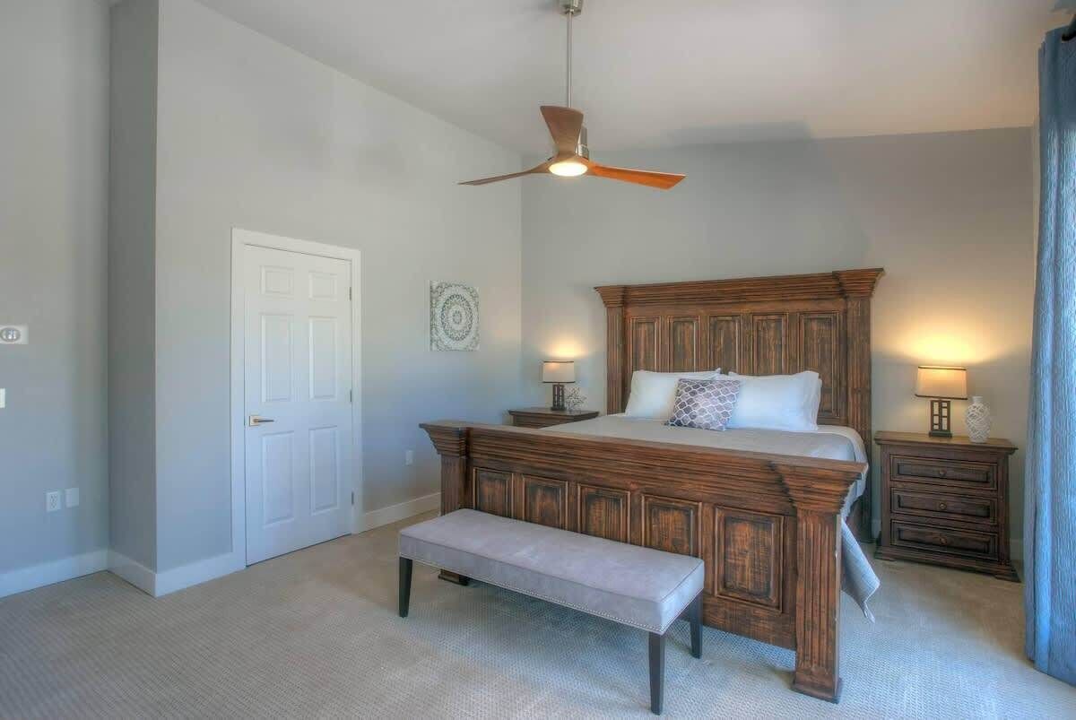 Een slaapkamer met een houten bed, een bankje, een plafondventilator en twee nachtkastjes met lampen.