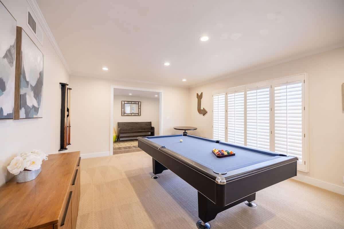A pool table in a well-lit room with a wooden bench and a framed picture on the wall.