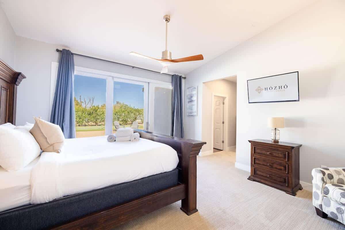 A bedroom with a large bed, a ceiling fan, a dresser, and a framed sign on the wall.