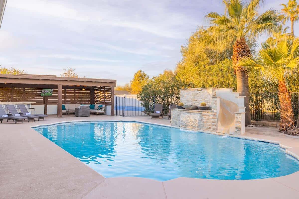 A swimming pool with lounge chairs and a covered seating area.