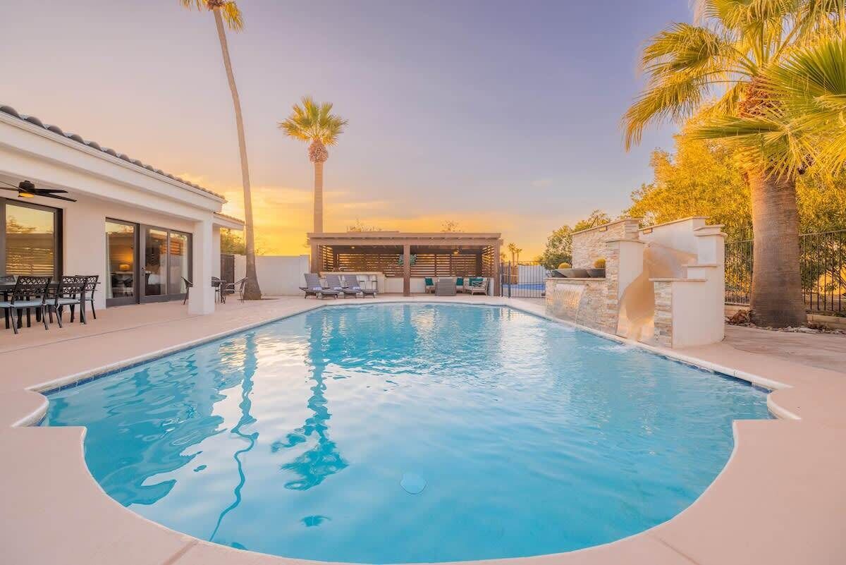 A swimming pool with lounge chairs, a covered seating area, and palm trees.