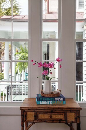 A window with a view of a white building and a palm tree. - Casa Zoë | Elegant 3BR Retreat Near King Street (Charleston)
