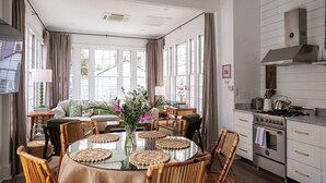 A dining area with a round glass table, surrounded by wicker chairs, and a kitchen with white cabinets and stainless steel appliances. - Casa Zoë | Elegant 3BR Retreat Near King Street (Charleston)