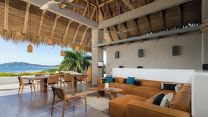 A spacious living area with a large sofa, wooden chairs, a dining table, and a view of the ocean. - Sunset House - oceanview villa 5-min walk to the beach by Elite Beach Villas (Tamarindo)
